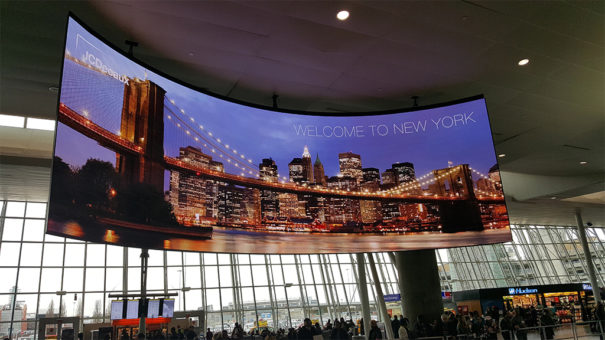 Large curved LED display showing New York City skyline in airport terminal